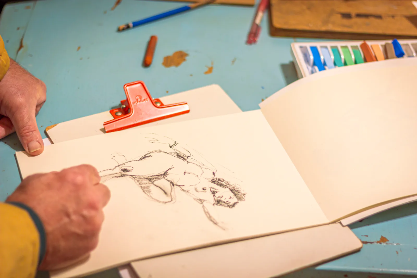 Mão desenhando uma figura humana em um caderno de papel claro.