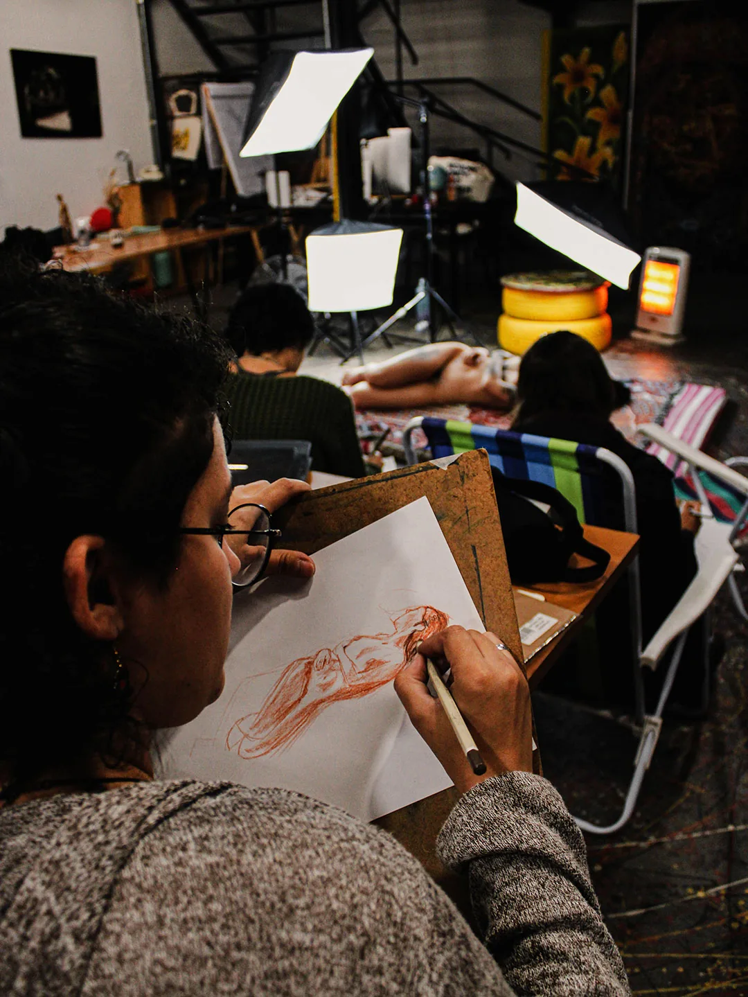 Participante desenhando em uma prancheta durante uma oficina de modelo vivo.